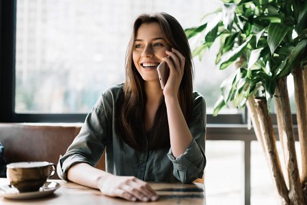 Uśmiechnięta kobieta biznesu rozmawiająca przez telefon w kawiarni – skalowanie firmy bez przestojów dzięki ofercie B2B.